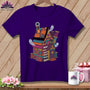 Purple t-shirt with a book-house, ghosts, and sewing notions graphic.