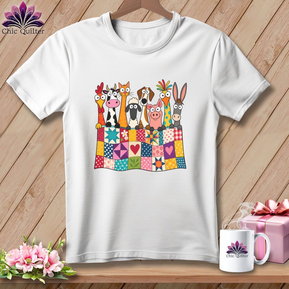A white t-shirt hanging on a wooden background, featuring a graphic of farm animals peeking over a colorful patchwork quilt.