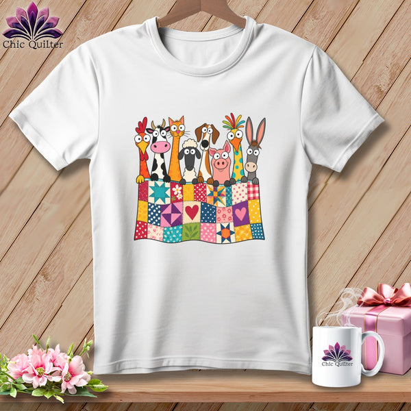A white t-shirt hanging on a wooden background, featuring a graphic of farm animals peeking over a colorful patchwork quilt.