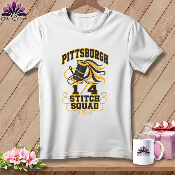 A white t-shirt on a wooden background features text reading "Pittsburgh 1/4 Stitch Squad" with a spool of thread graphic.