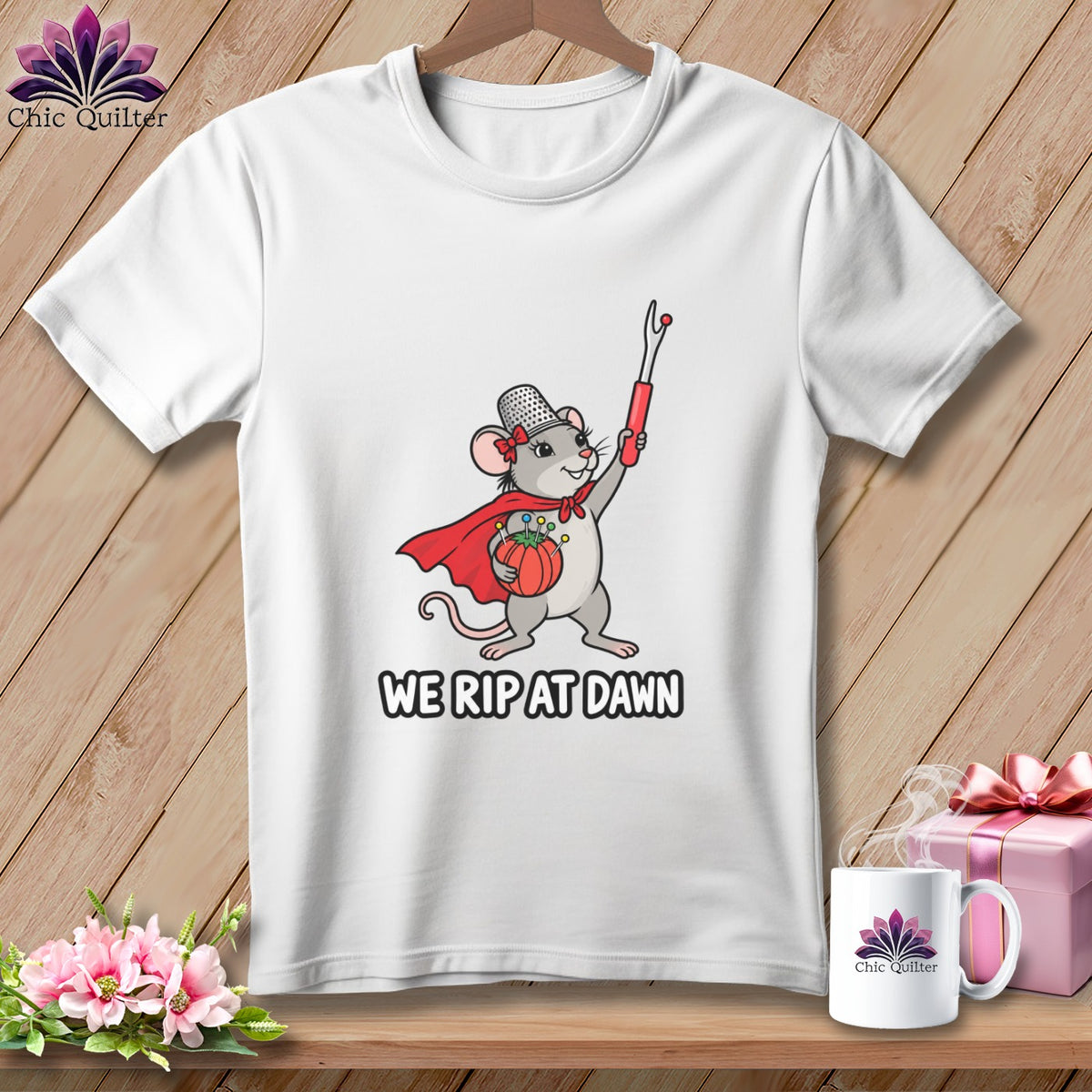 White t-shirt featuring a cartoon mouse wearing a cape and thimble, holding a seam ripper and pincushion, with the text WE RIP AT DAWN.