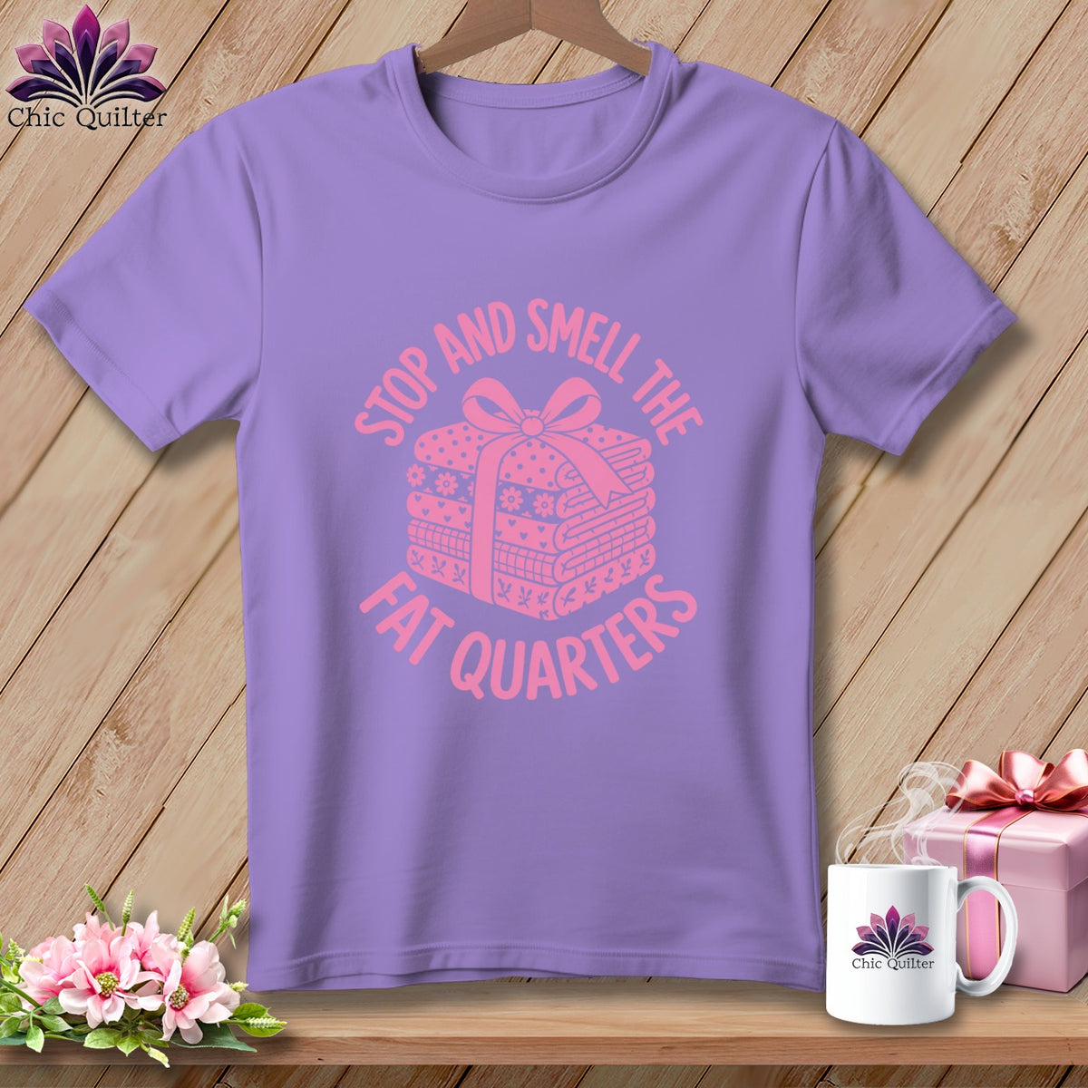 A purple t-shirt printed with a pink graphic of folded fabric tied with a ribbon and the text Stop and Smell the Fat Quarters.