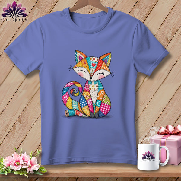 Periwinkle blue t-shirt with a colorful patchwork fox graphic hanging on a wooden background.