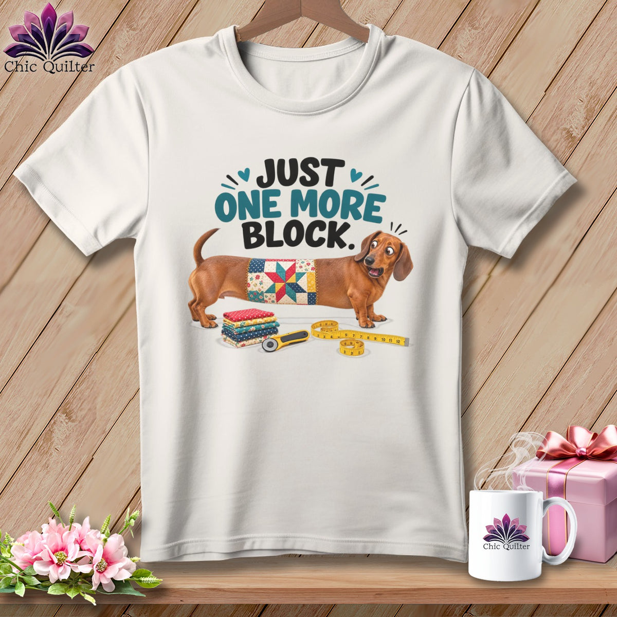 White t-shirt with dachshund, quilt square, fabric stacks, rotary cutter, and measuring tape.