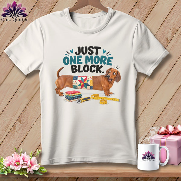 White t-shirt with dachshund, quilt square, fabric stacks, rotary cutter, and measuring tape.