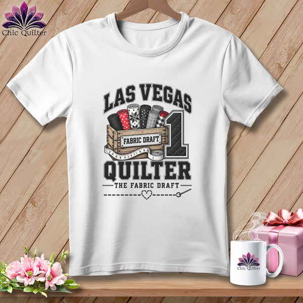 A white crewneck t-shirt featuring a quilting graphic with Las Vegas Quilter text, hanging on a wooden background.