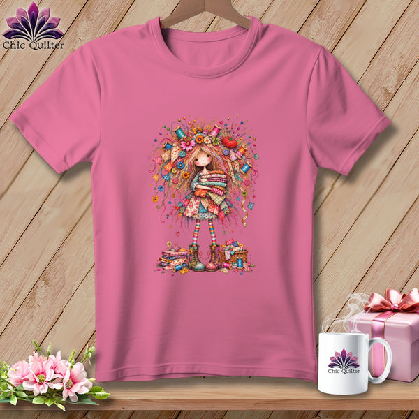 A pink crew-neck t-shirt featuring a whimsical illustration of a girl surrounded by sewing supplies.