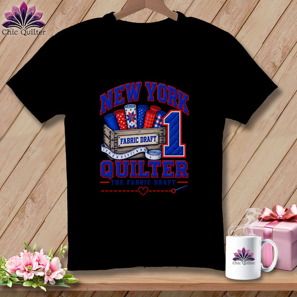 Black t-shirt featuring a New York Quilter graphic with fabric rolls, a measuring tape, and text.