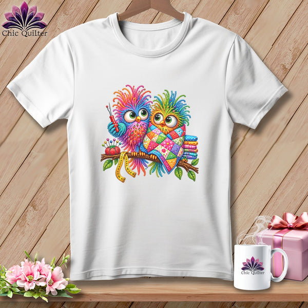 A white crew-neck t-shirt featuring a colorful graphic of two whimsical owls perched on a branch.