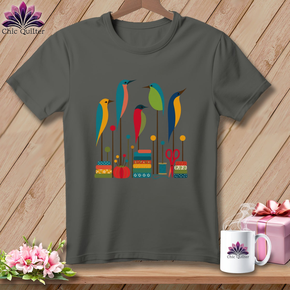 A charcoal gray crewneck t-shirt featuring a graphic illustration of five colorful birds perched among sewing notions.