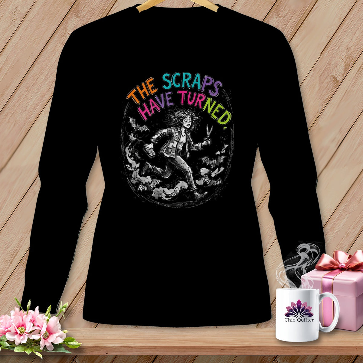 Black t-shirt with a circular graphic of a woman running, holding scissors, with text "THE SCRAPS HAVE TURNED".