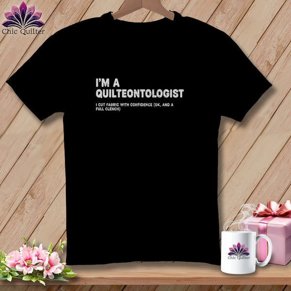 Black t-shirt with "I'M A QUILTEONTOLOGIST" and "I CUT FABRIC WITH CONFIDENCE (OK, AND A FULL CLENCH)" text.