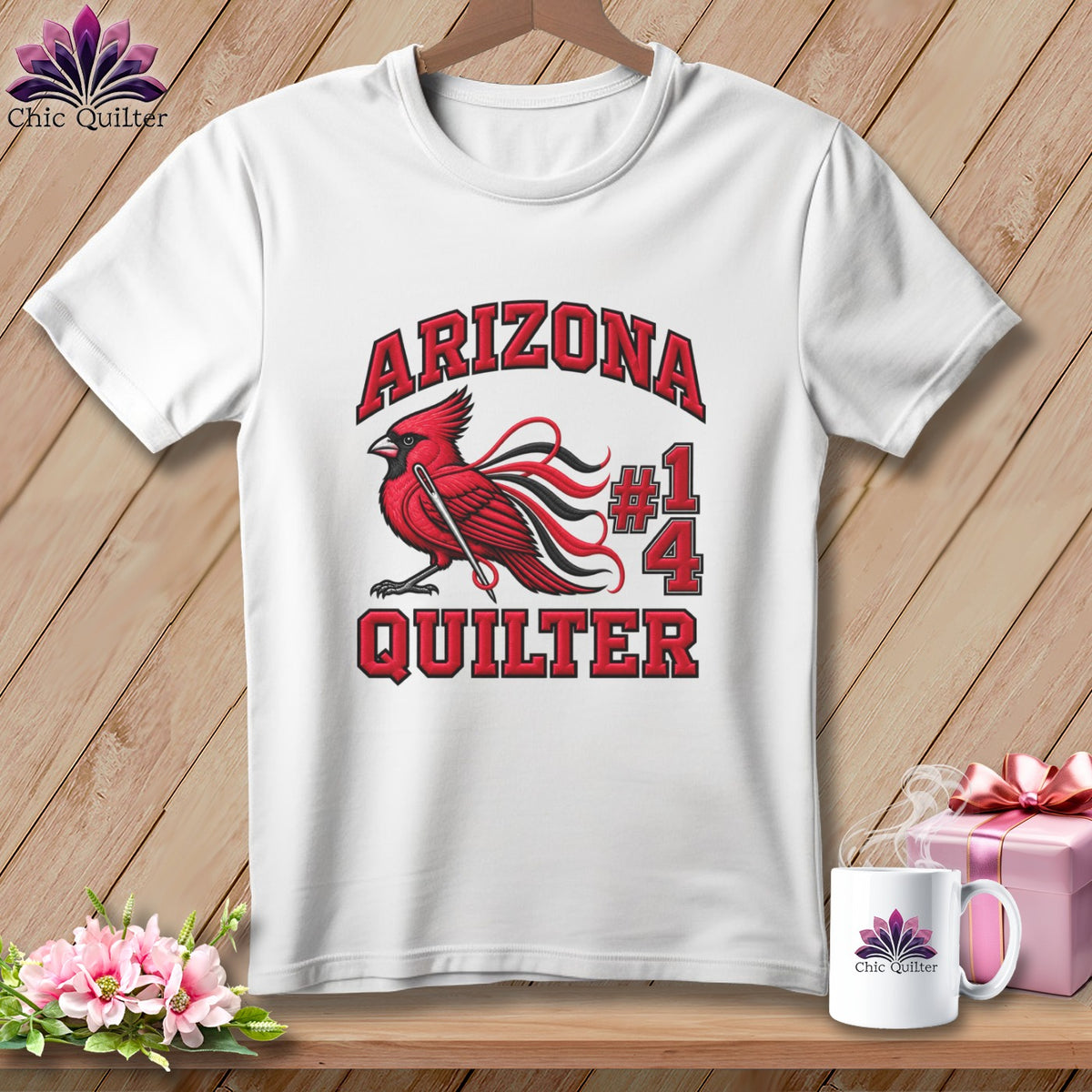 A white t-shirt hanging on a wooden background features a graphic of a red cardinal and the text Arizona Quilter #14.