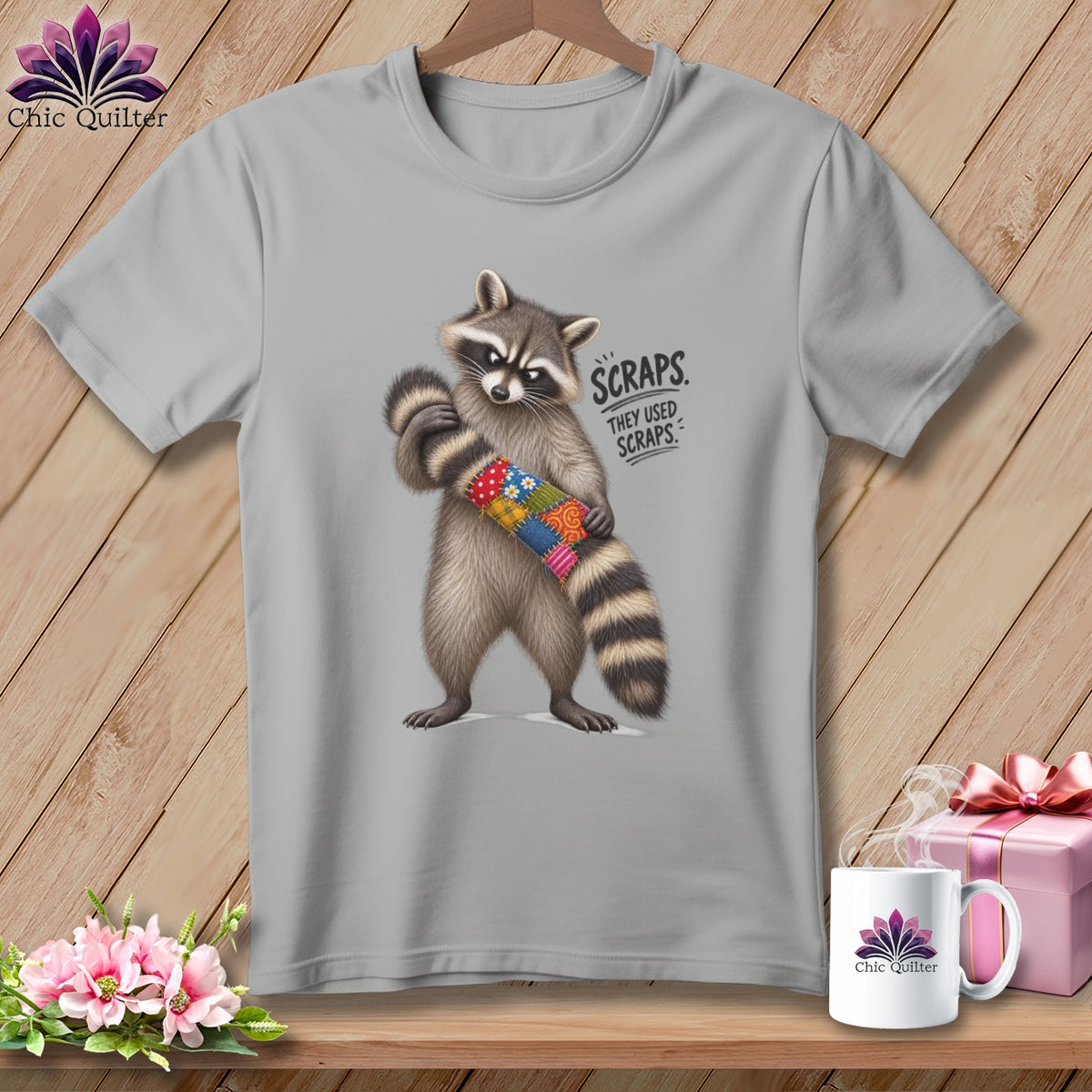 Gray t-shirt with raccoon holding a patchwork tube, reads "Scraps. They Used Scraps."