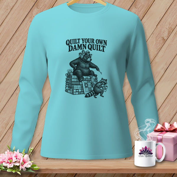 Light blue long-sleeve t-shirt with a graphic of a bear and raccoon quilting and the text Quilt Your Own Damn Quilt.