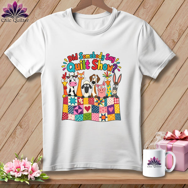 A white t-shirt featuring a cartoon design of farm animals behind a colorful quilt, with the text Did Somebody Say Quilt Show.