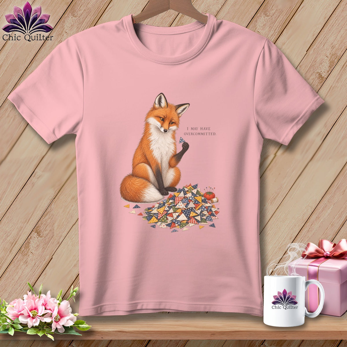 Pink t-shirt with a fox holding a patchwork triangle, text "I MAY HAVE OVERCOMMITTED."