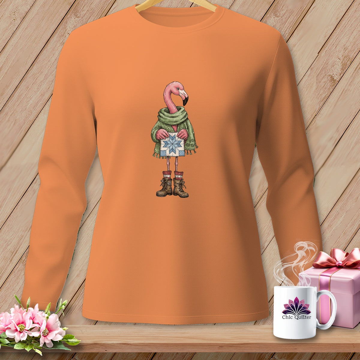 Flamingo wearing scarf and boots holding a blue star gift box on orange shirt.