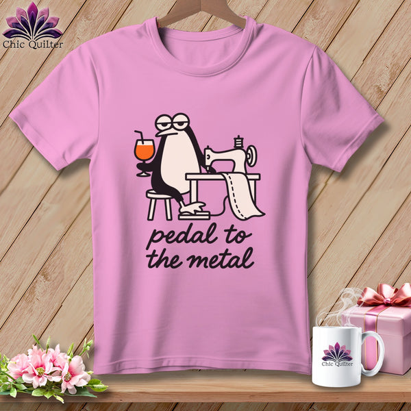 Pink t-shirt with cartoon penguin sewing, holding a drink, text "pedal to the metal".