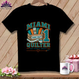 Black t-shirt featuring a Miami Quilter graphic with a wooden crate of fabric rolls and a large number one.
