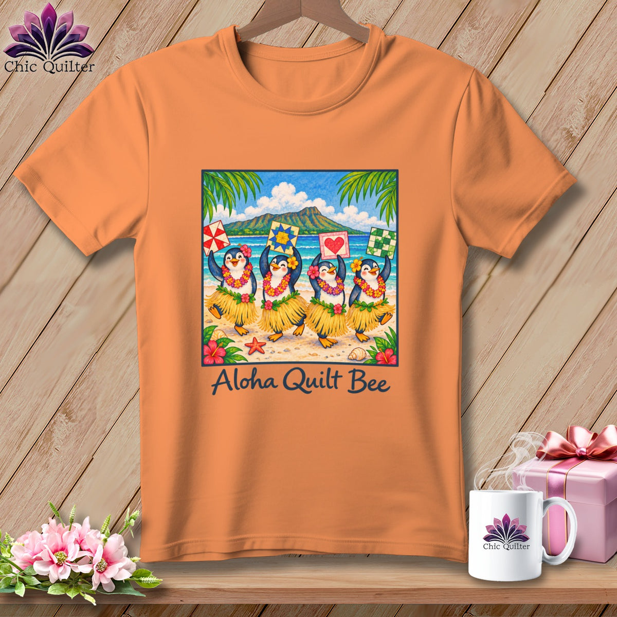 Orange t-shirt featuring a graphic of four hula-dancing penguins on a beach, text reading Aloha Quilt Bee.