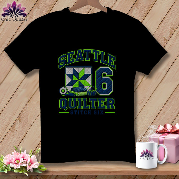 Black short-sleeved t-shirt with Seattle Quilter and number six graphics, displayed on a wooden background.