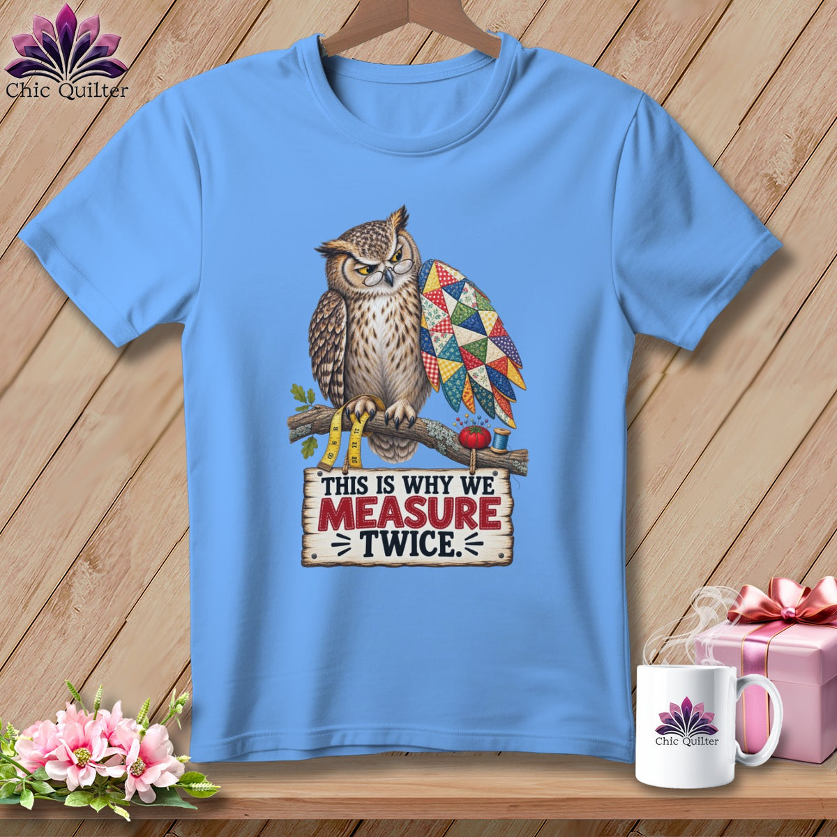 Light blue t-shirt with owl holding a quilt and text "This is why we measure twice."
