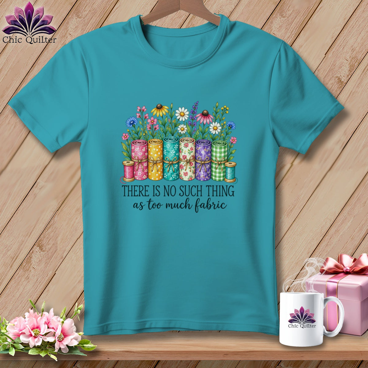 Teal t-shirt featuring a graphic of colorful fabric rolls, wildflowers, and the text There is no such thing as too much fabric.