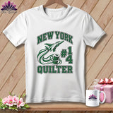 A white t-shirt hanging on a wooden background, featuring green text that reads New York Quilter, a spool of thread, and a jet plane.