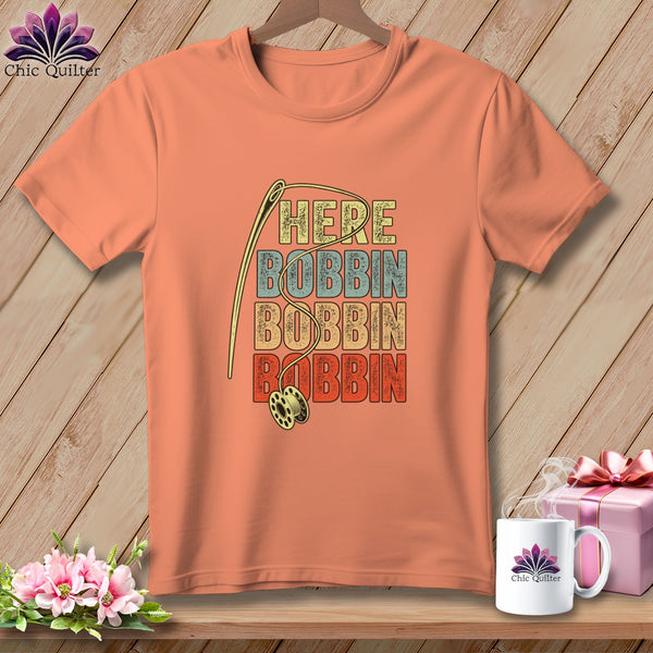 Peach t-shirt with "HERE BOBBIN BOBBIN BOBBIN" text and sewing needle and bobbin graphic.