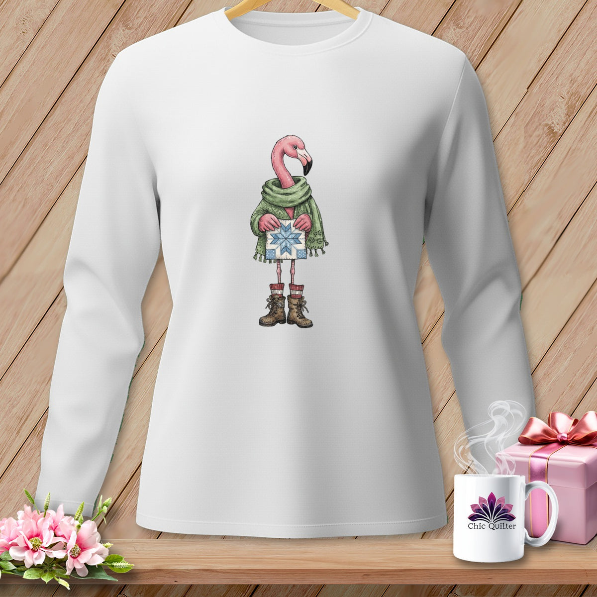 White long-sleeve shirt with a cartoon flamingo wearing a scarf, boots, and holding a gift.
