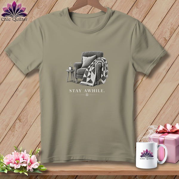 T-shirt graphic of armchair, quilt, and "STAY AWHILE." text.