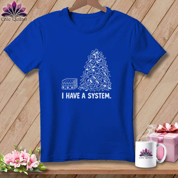 Blue t-shirt with stacked fabric and chaotic fabric pile graphic and text "I HAVE A SYSTEM."