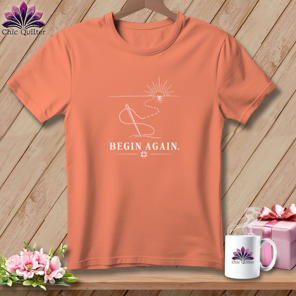 Coral t-shirt with needle, thread, sunrise, and "BEGIN AGAIN" text.