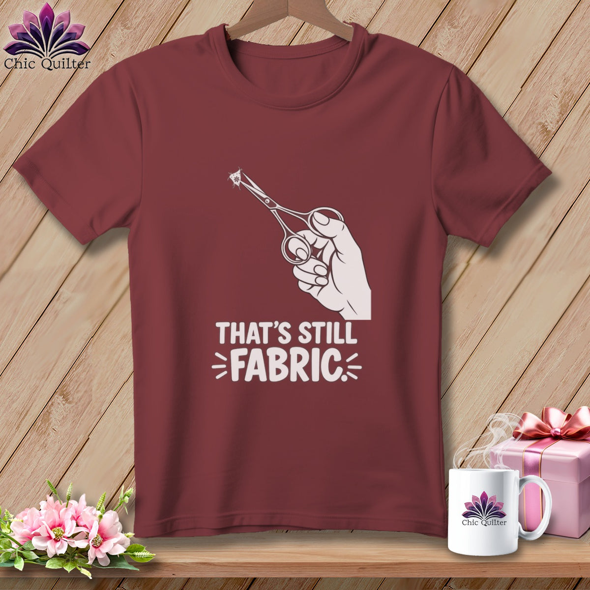 Maroon t-shirt with white graphic of a hand holding scissors cutting fabric.
