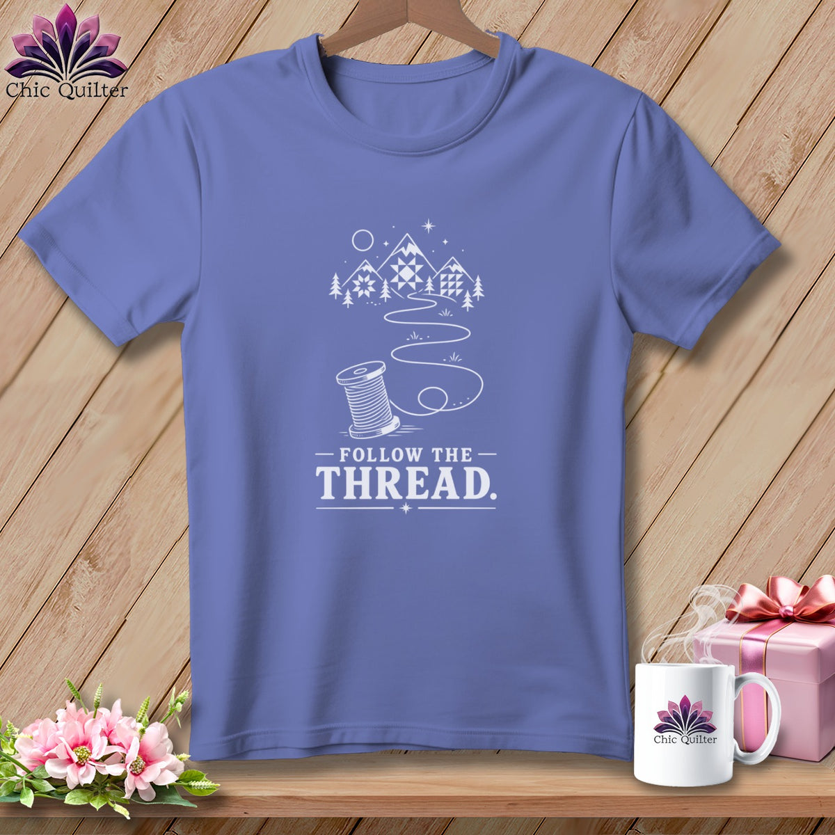 Periwinkle t-shirt with "Follow the Thread" design and spool of thread.