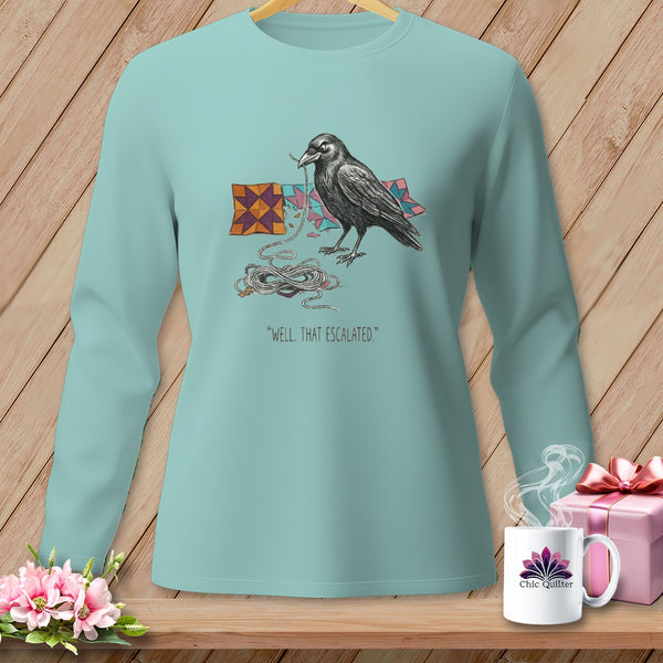 Light blue long-sleeved shirt with a crow holding string and quilt pieces, text reads "WELL. THAT ESCALATED."