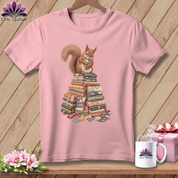 Pink t-shirt with a squirrel holding a fabric heart atop a stack of quilting fabric.