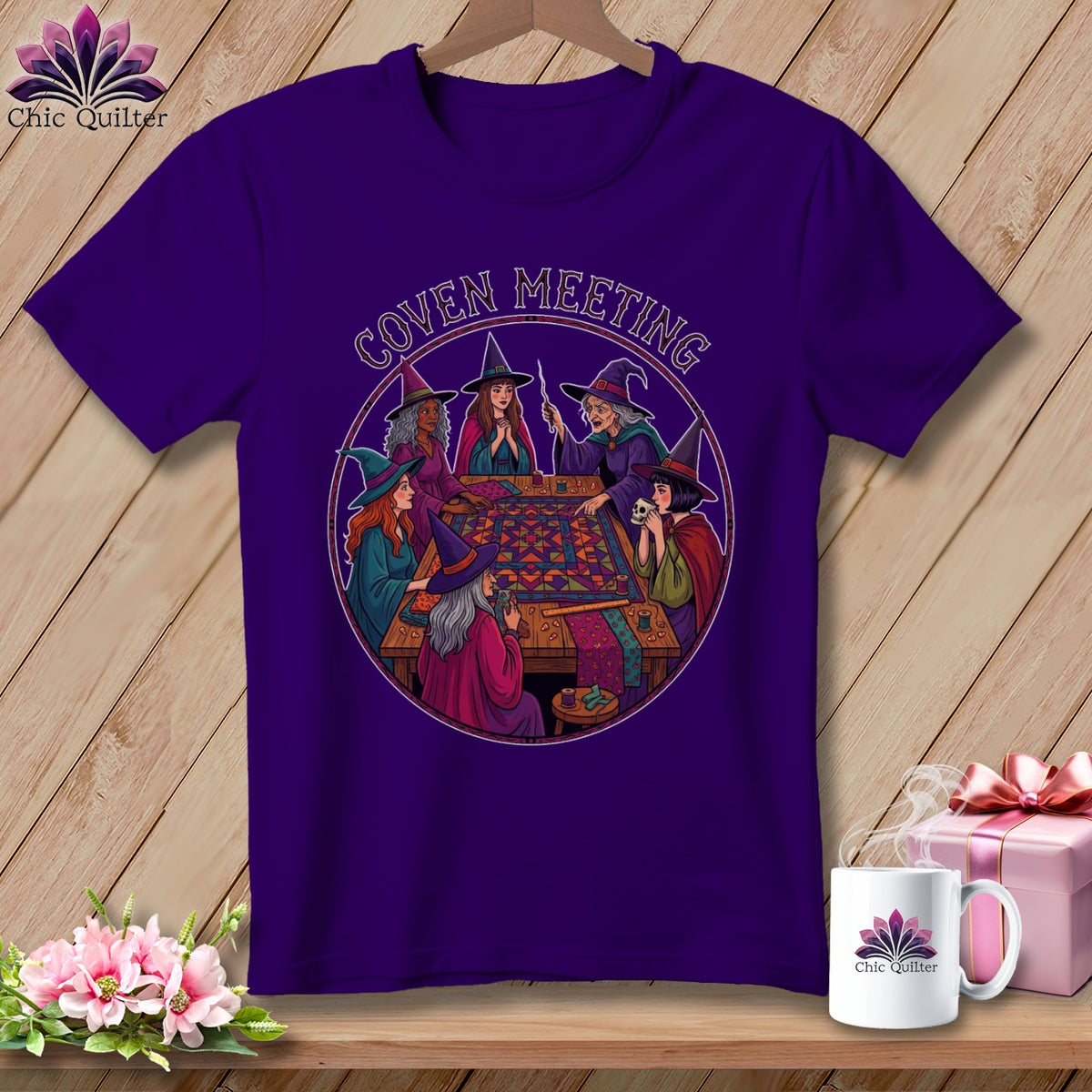 Purple t-shirt with graphic of witches sewing around a quilt, text "Coven Meeting".