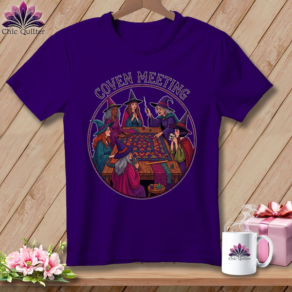 Purple t-shirt with graphic of witches sewing around a quilt, text "Coven Meeting".
