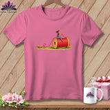 Pink short-sleeved t-shirt with a graphic of a woman riding a giant red thread spool on grass.