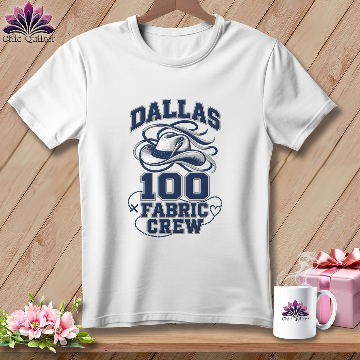 A white t-shirt on a wooden hanger features blue text reading Dallas 100 Fabric Crew with a cowboy hat graphic.