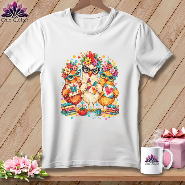 A white t-shirt features a colorful graphic of three chickens wearing glasses and floral crowns, holding quilt blocks.