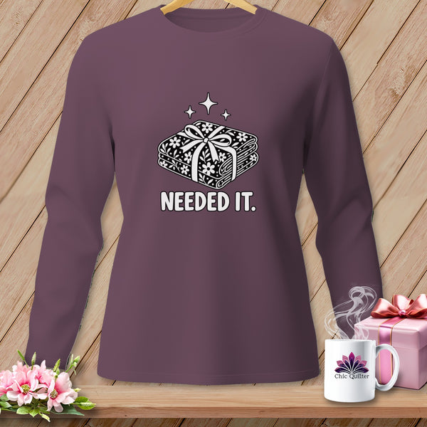 Purple long-sleeve shirt with a graphic of stacked fabric bundles and the text "NEEDED IT."