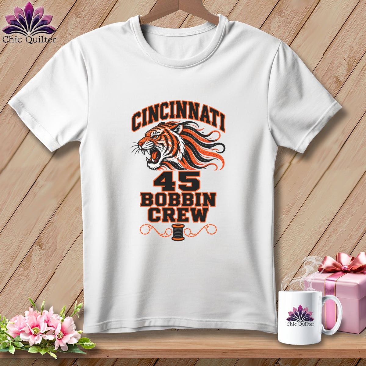 White t-shirt featuring a tiger graphic and text reading Cincinnati 45 Bobbin Crew, displayed on a wooden background.