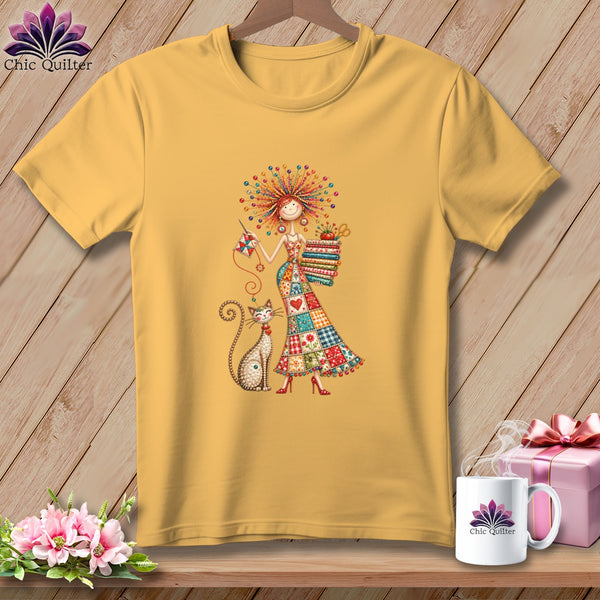 Gold t-shirt featuring a whimsical illustration of a woman in a patchwork dress with a cat.