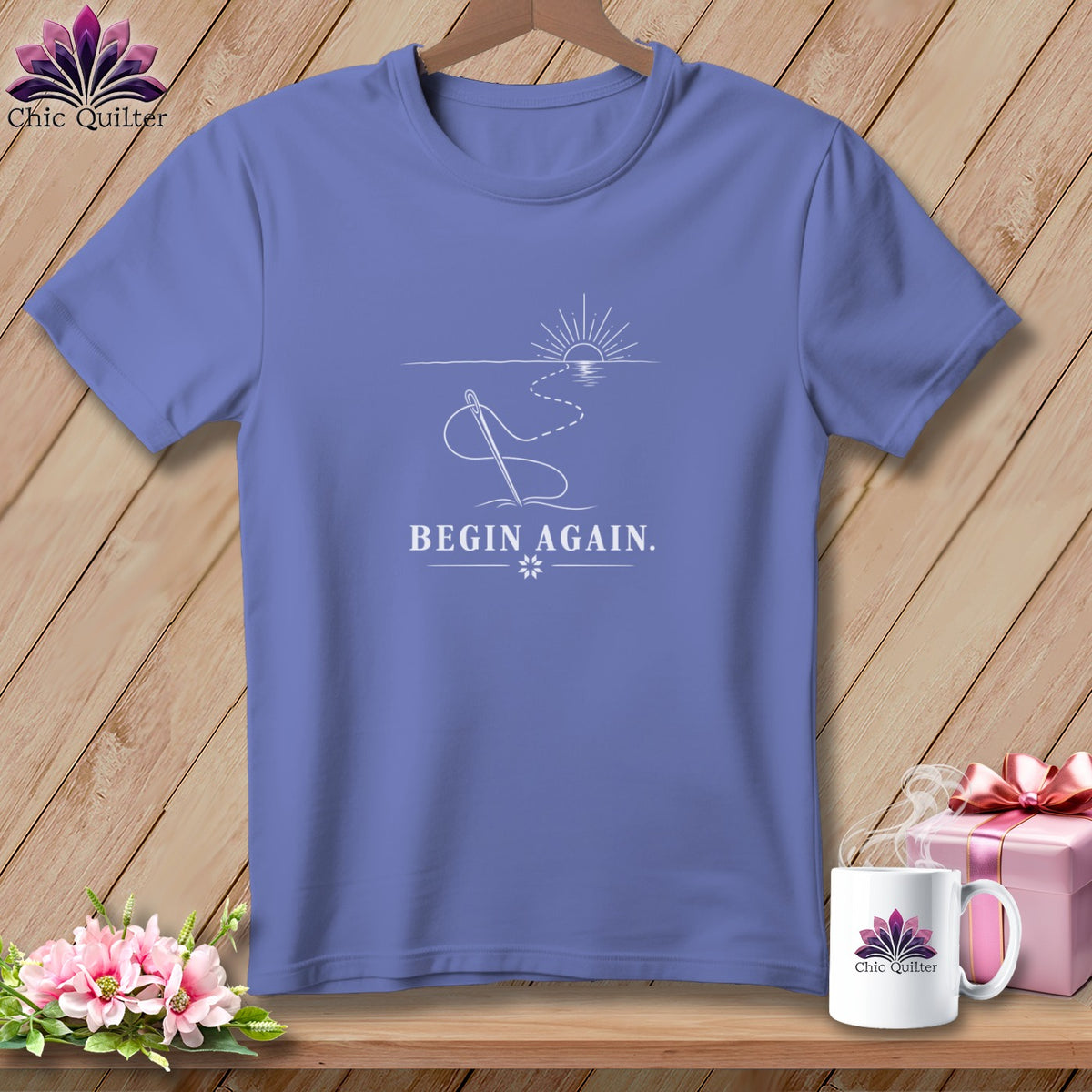 Periwinkle t-shirt with needle and thread graphic and "BEGIN AGAIN." text.