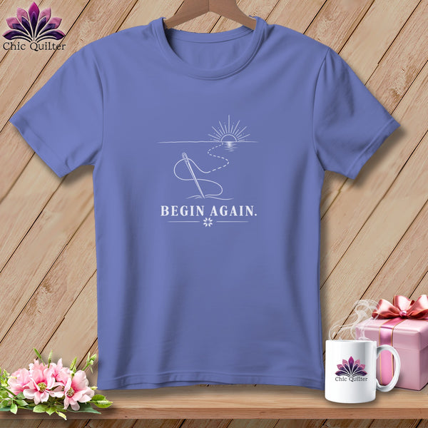 Periwinkle t-shirt with needle and thread graphic and "BEGIN AGAIN." text.
