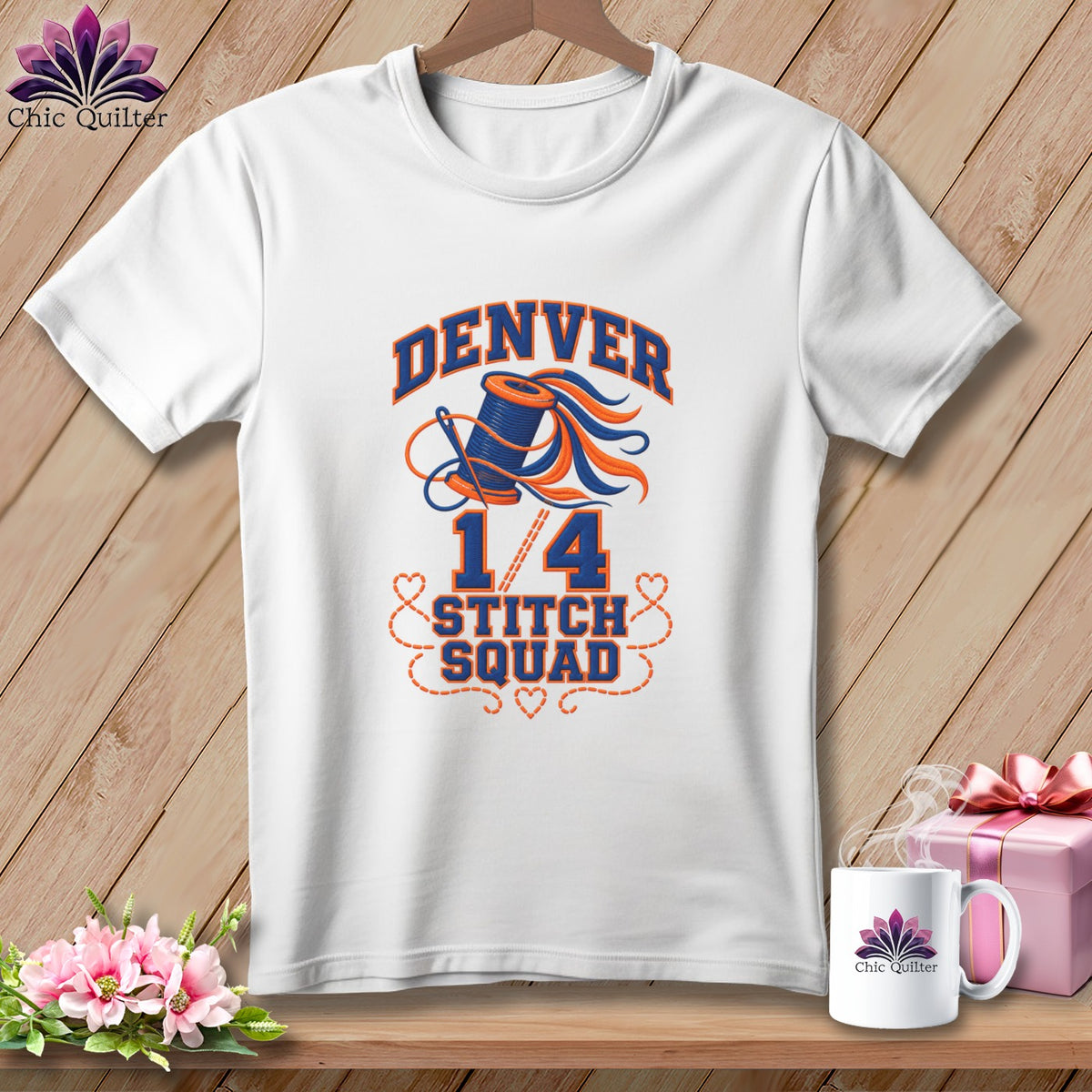 White t-shirt with a blue and orange Denver 1/4 Stitch Squad sewing graphic hanging on wooden background.