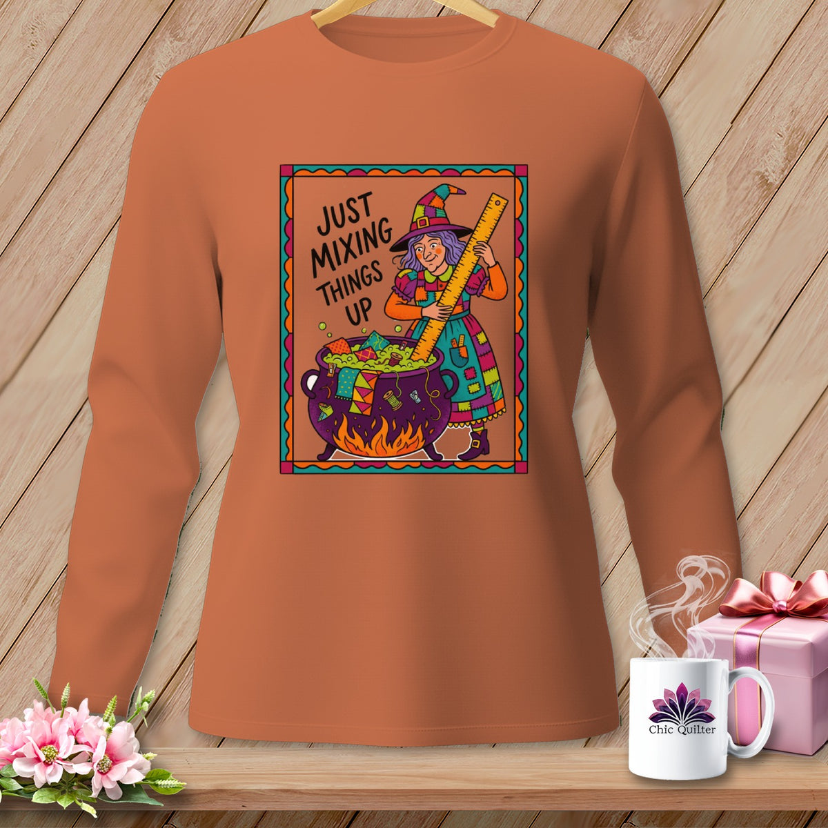 Orange long-sleeve shirt with a witch mixing a cauldron, text says "JUST MIXING THINGS UP".
